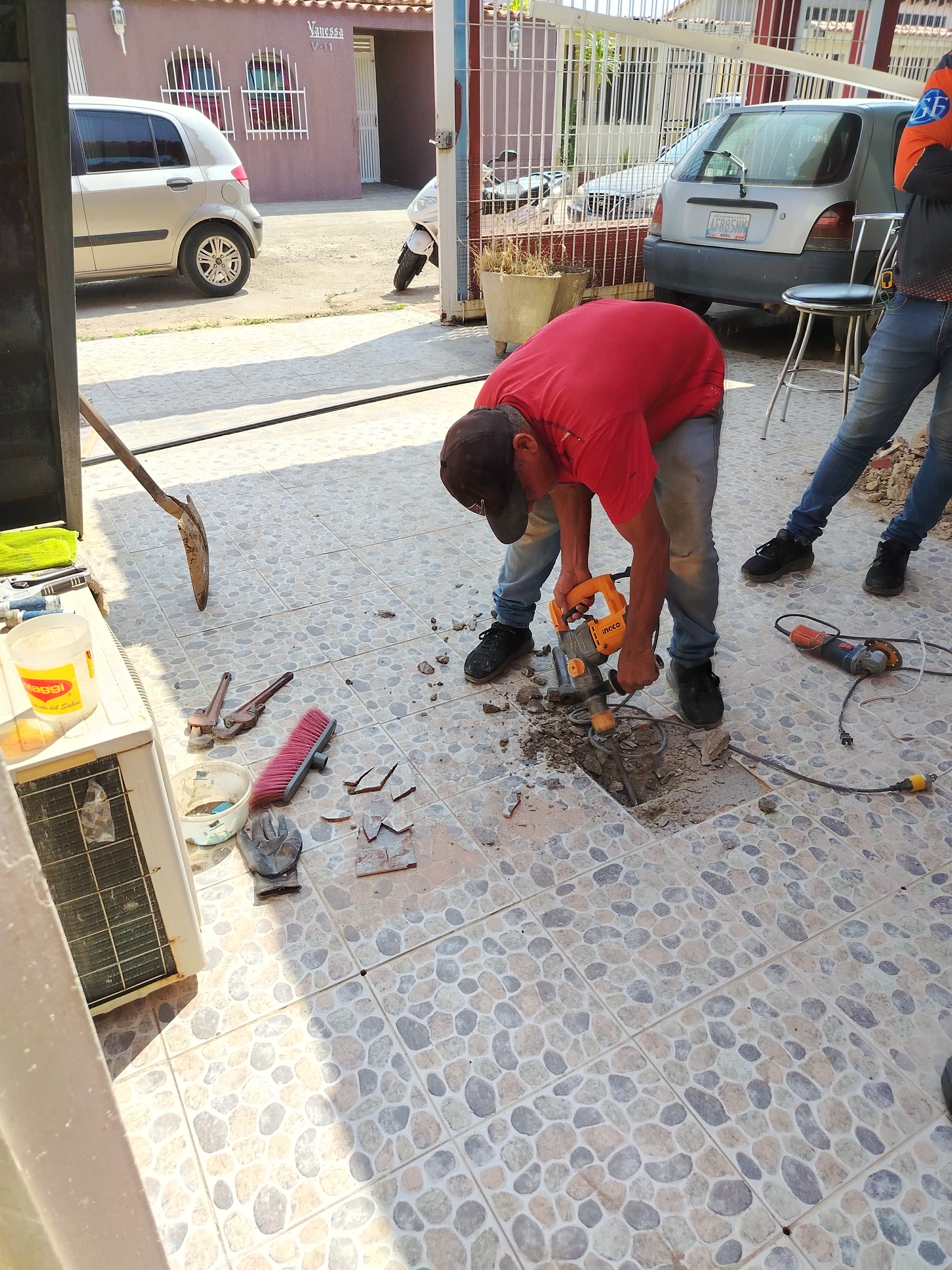 Trabajador con camisa roja rompe baldosas de un patio usando un martillo demoledor eléctrico.